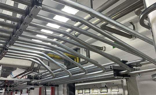 Industrielle Hydraulikverrohrung mit parallel verlegten Rohrleitungen unter der Hallendecke einer Hydraulikanlage.